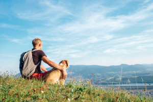 Man with his beagle dog sits on the top of hill over the mountai