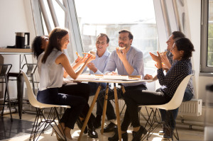 Friendly happy diverse workers laughing eating pizza together in